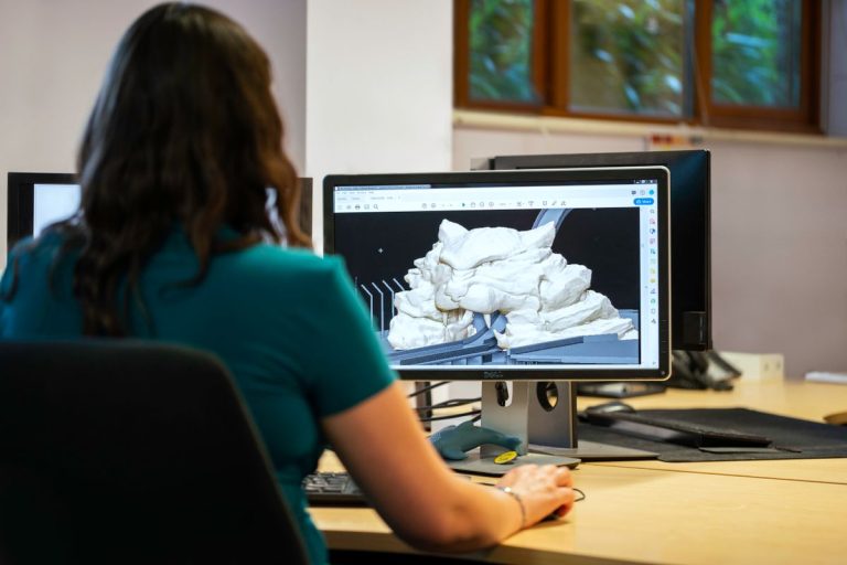 A woman using CAD software for 3D modeling in an office setting with a back view