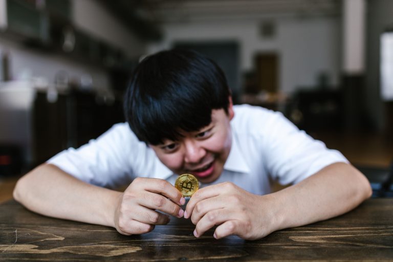 A young man excitedly examining a Bitcoin coin in an indoor setting