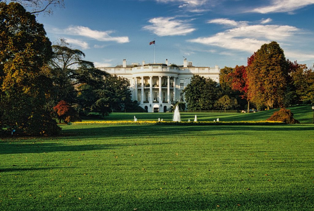 White House south facade beyond a lawn and fountain, surrounded by autumn trees